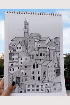 a hand holding up a drawing of a city