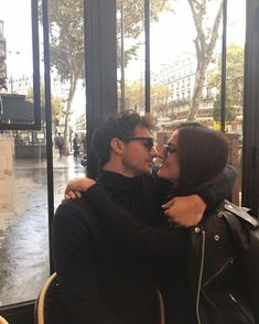 a man and woman sitting next to each other in front of a glass window on a rainy day