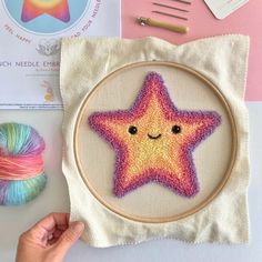 a hand is holding a cross - stitch star in front of some yarn and scissors