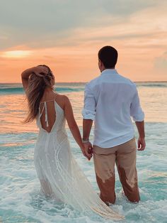 a man and woman holding hands walking into the ocean