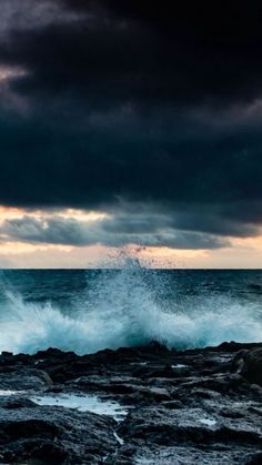 the waves are crashing on the rocks by the water's edge at night time