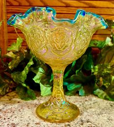 a yellow glass bowl sitting on top of a table next to green plants and leaves