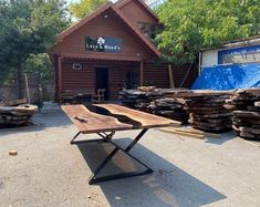 a wooden table sitting in front of a building with lots of wood stacked on top of it