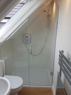 a bathroom with a glass shower door next to a toilet under a slanted roof