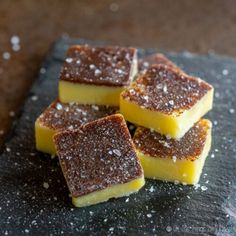 four pieces of yellow cake sitting on top of a black slate board with sugar sprinkles