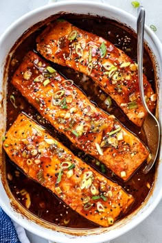 baked salmon with sesame seeds and seasoning in a white casserole dish next to a spoon