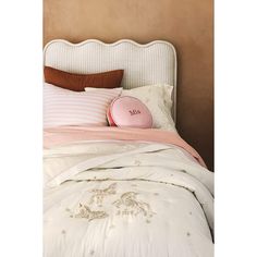 a white bed with pink and brown pillows on it's headboard next to a beige wall