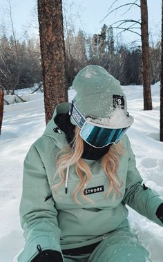 a woman sitting in the snow with her skis on and she is wearing a helmet