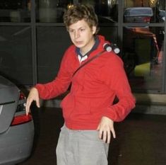 a young man standing in front of a car with his hand on the door handle