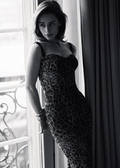 a woman in a leopard print dress leaning against a window with her hands on her hips