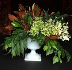 a vase filled with lots of green and white flowers on top of a black table