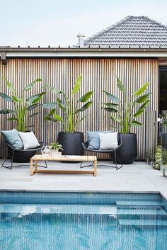 an outdoor living area with chairs, tables and a pool in front of a wooden fence