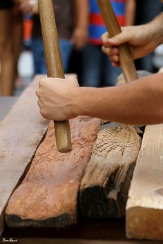 two hands holding wooden sticks over wood planks on a table with people in the background