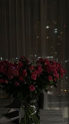 a vase filled with red roses sitting on top of a table next to a window