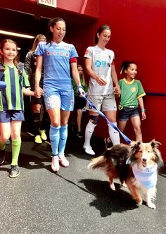 a group of young people walking down a street with a small dog on a leash