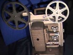 an old movie projector sitting on top of a black table next to a blue wall