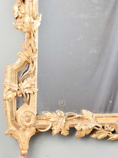 an ornate gold framed mirror with flowers and leaves on the frame, against a gray wall