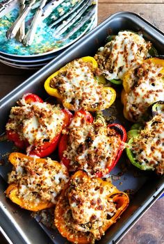 stuffed bell peppers in a baking pan with cheese on top and other dishes behind them