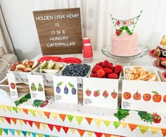 a table topped with lots of food next to a sign that says holiday kep is one hungry caterpillar