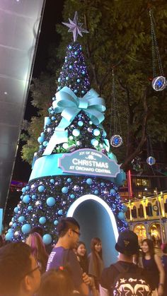 people standing around a christmas tree in the middle of a city at night with lights and decorations on it