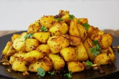 a pile of fried potatoes on a black plate with cilantro sprigs