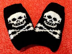 a pair of black and white knitted mittens with skulls on them sitting on a red surface