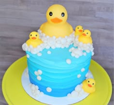 a blue cake with rubber ducks in the bathtub and bubbles around it on a yellow plate