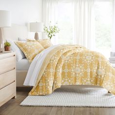 a bed with yellow and white comforters in a bedroom next to a window,