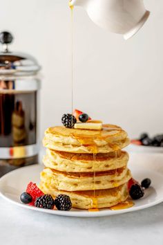 a stack of pancakes with syrup being drizzled over them and topped with berries