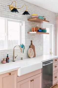 a kitchen with pink cabinets and white brick walls, along with open shelving above the sink