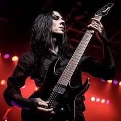 a man with long black hair playing an electric guitar