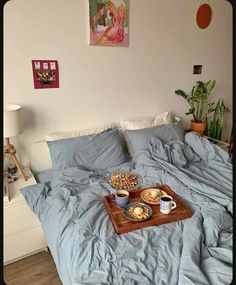 a tray with food on it sitting on top of a bed next to a painting