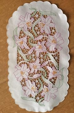 a white doily with pink flowers on it sitting on top of a wooden table