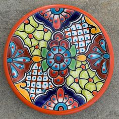 an orange plate with colorful designs on it sitting on the ground next to a sidewalk