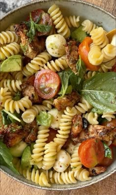 a bowl filled with pasta and vegetables on top of a wooden table