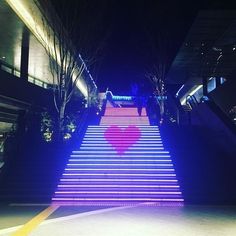 the stairs are lit up with pink and blue lights in the night time, as well as trees