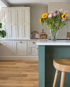 a vase filled with yellow and purple flowers on top of a kitchen counter next to a wooden stool