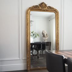 a large gold framed mirror sitting on top of a wooden table next to a dining room table