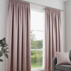 a living room with pink curtains and a grey chair in front of a window that is open