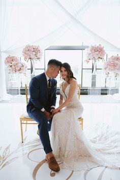 a bride and groom sitting on a chair in the middle of a room with flowers