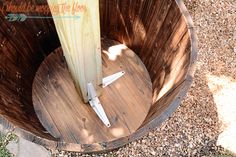 a surfboard sticking out of the side of a wooden barrel on top of gravel