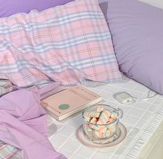 an unmade bed with pink and blue sheets, plaid pillow cases, and a bowl of marshmallows on it