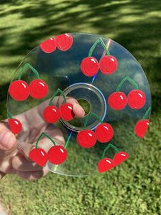 a person holding a glass with cherries on it in front of some grass and trees