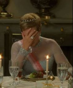 a woman wearing a tiara sitting at a table with candles in front of her