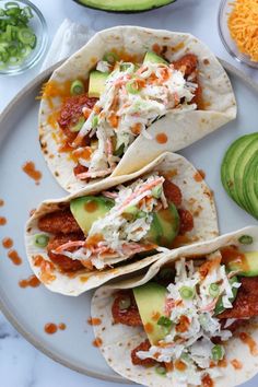 three tacos on a plate with avocado and salsa