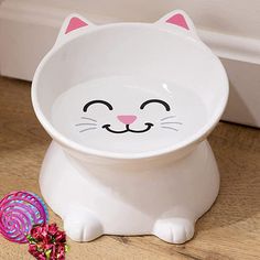 a white cat shaped bowl sitting on top of a wooden floor next to a candy lollipop