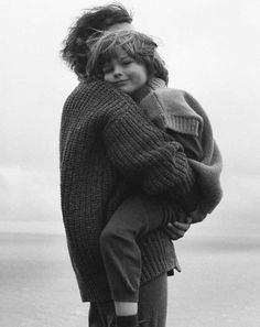 black and white photograph of a woman holding a child in her arms by the ocean