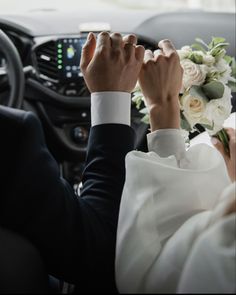 the bride and groom are sitting in their car together, holding hands over the steering wheel