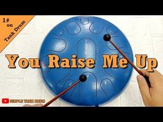 a person holding two sticks in front of a blue frisbee with the words you raise me up on it