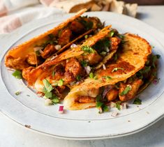 some tacos are stacked on top of each other on a white plate with green garnishes